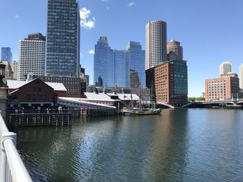 Modern buildings by river against sky in city