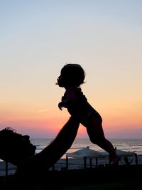 Silhouette boy standing on beach against clear sky during sunset