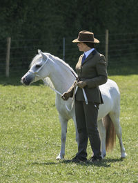 Woman in suit standing by pony on grassy field