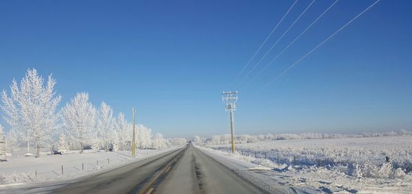 Empty road amidst snowcapped landscape against clear blue sky