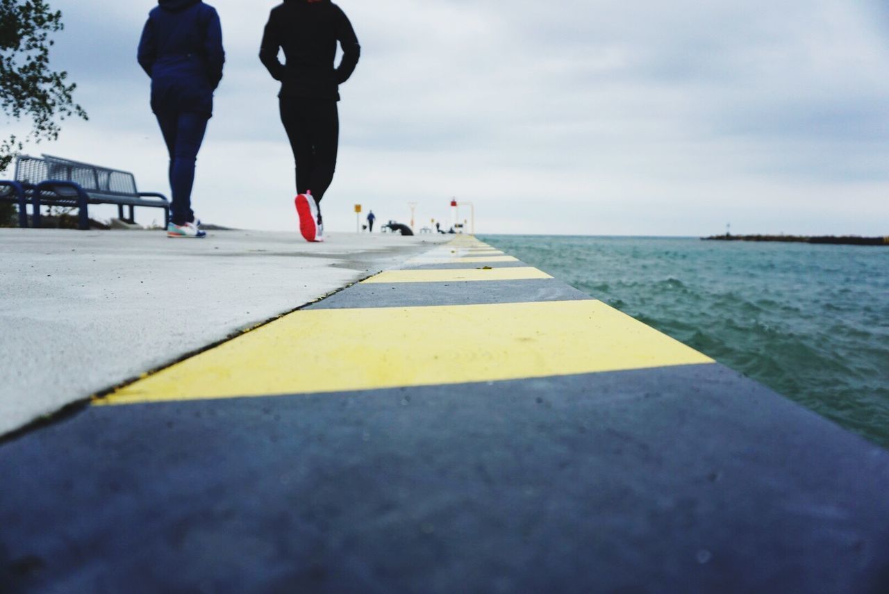 REAR VIEW LOW SECTION OF WOMAN WALKING AT SEA SHORE