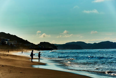 People fishing on beach against sky in the morning