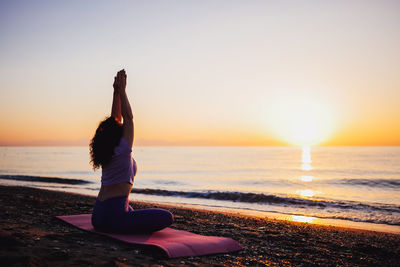 Rear view of woman standing at beach against sky during sunset