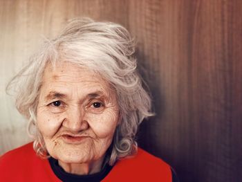 Close-up portrait of smiling senior woman against wall