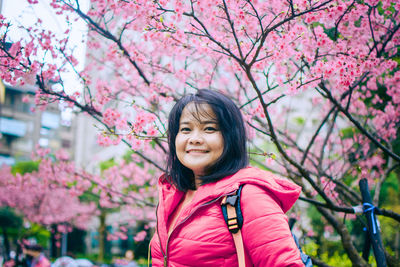 Portrait of smiling woman with pink cherry blossoms against trees