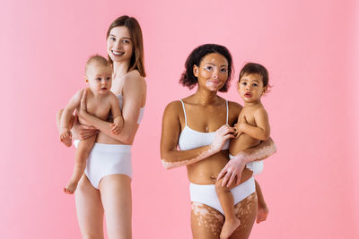 Portrait of female friends standing against pink background