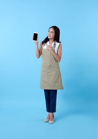Full length of young woman using mobile phone against blue background