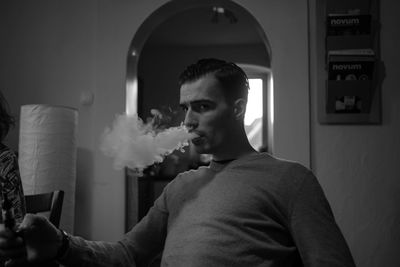 Portrait of young man smoking cigarette while sitting at home