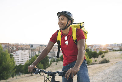 Happy delivery man looking away while sitting on bicycle