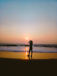 Silhouette woman standing on beach against sky during sunset