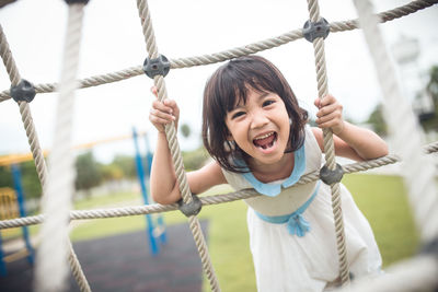 Portrait of girl screaming while leaning on jungle gym in playground