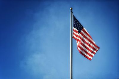 Low angle view of american flag on pole against blue sky