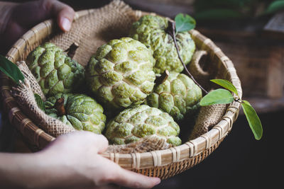 Cropped hands holding custard apples in basket