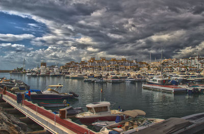 Boats in harbor against cloudy sky