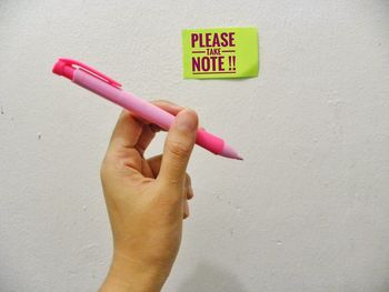 Cropped hand holding pen by adhesive note with text on wall