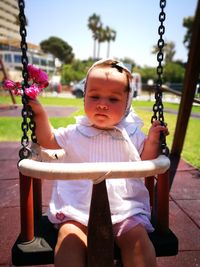 Cute baby girl holding flowers while sitting on swing in playground