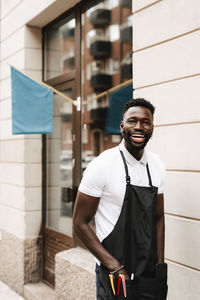 Portrait of cheerful male hairdresser standing outside barber shop