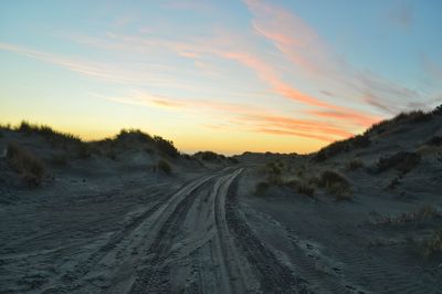 Tire tracks on road against sky during sunset