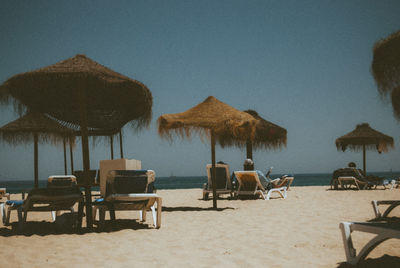 Lounge chairs on beach against clear sky