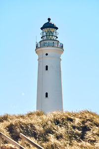 Lighthouse by sea against clear blue sky