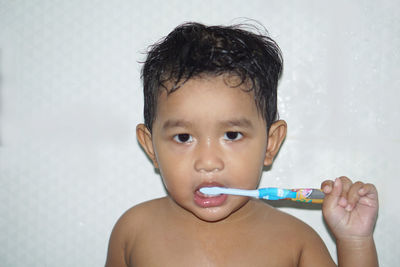 Portrait of shirtless baby boy brushing teeth in bathroom