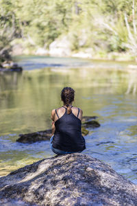 Rear view of woman sitting on rock by lake