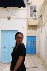 Portrait of young woman standing against building