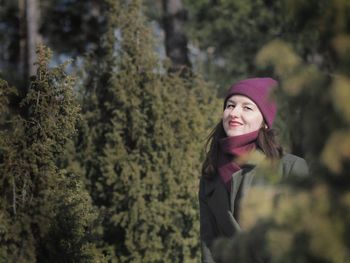 Portrait of smiling young woman standing against trees