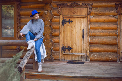  village woman in a blue hat sits at a wooden house in autumn