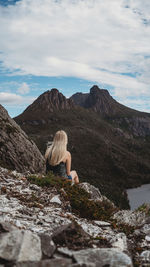 Rear view of woman sitting on rock against sky