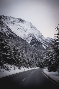 Road by mountains against clear sky during winter