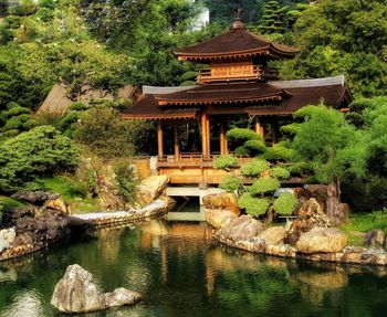 Temple by lake and building against trees