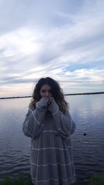 Portrait of woman drinking coffee against lake and cloudy sky