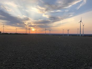 Wind turbines on field against sky during sunset