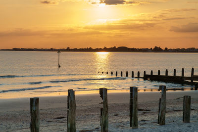 Wooden posts on beach against sky during sunset