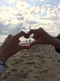 Cropped image of woman forming heart shape with hands at beach