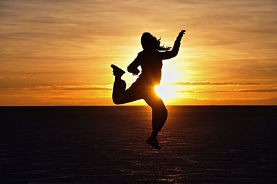 Silhouette of person jumping against sky at sunset
