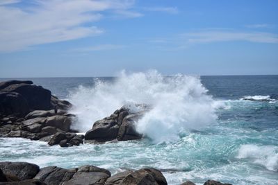 Waves breaking on rocks against blue sky