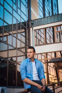 Young man looking away while standing against building