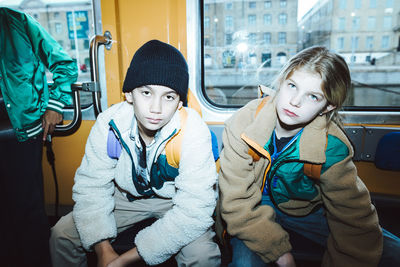 Portrait of boy and girl sitting while traveling in tram on weekend