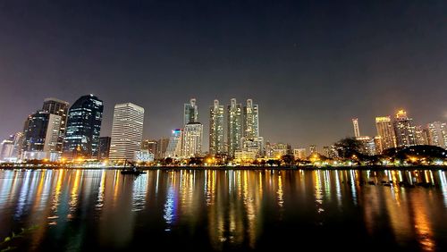 Illuminated buildings by river against sky at night