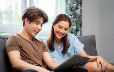 Friends using digital tablet while sitting on sofa at home