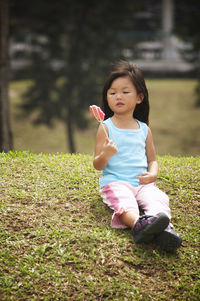 Girl with candy sitting on grassy field at park