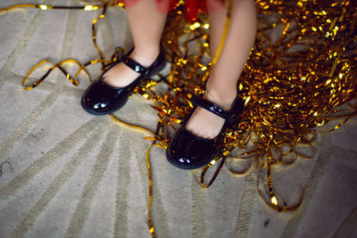 Children feet in black sandals stands on a carpet with gold decor ribbons. close up