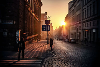 Road amidst buildings against sky during sunset