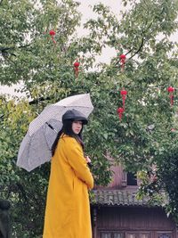 Woman standing by flowering plants against trees