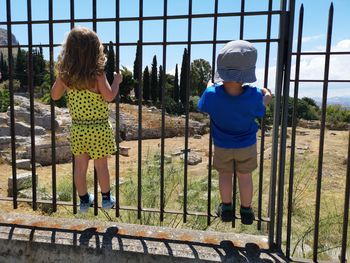 Rear view of siblings standing by fence