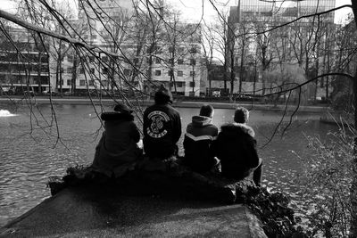 Rear view of people sitting by canal during winter