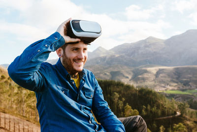 Portrait of smiling young man using smart phone against mountains