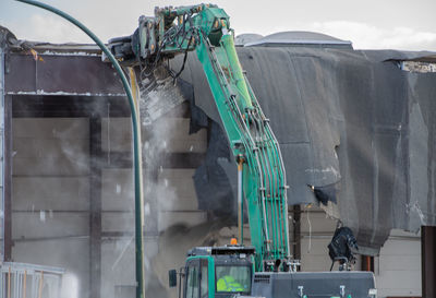 Excavator demolishing factory against sky